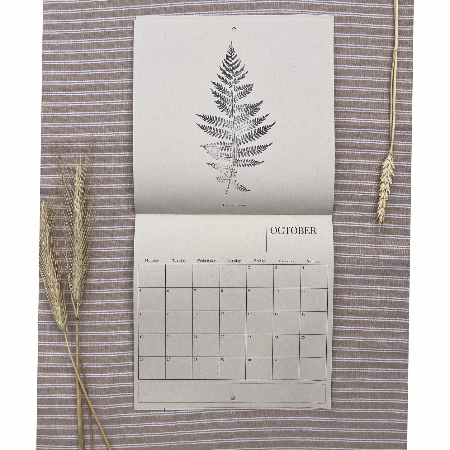 Calendar with a fern design on a textured surface with wheat stalks.