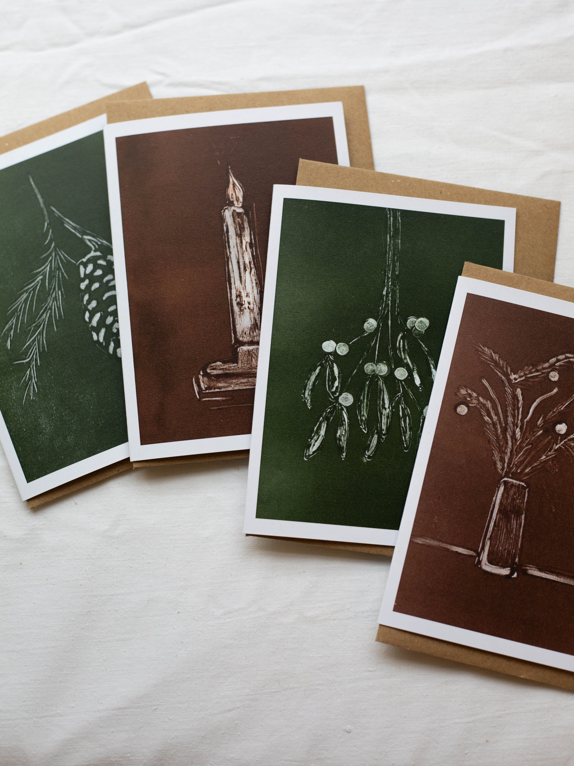 A pack of four Christmas cards with monotype drawings, featuring designs such as mistletoe, Christmas foliage, pine, and a candlestick, displayed on a white background.
