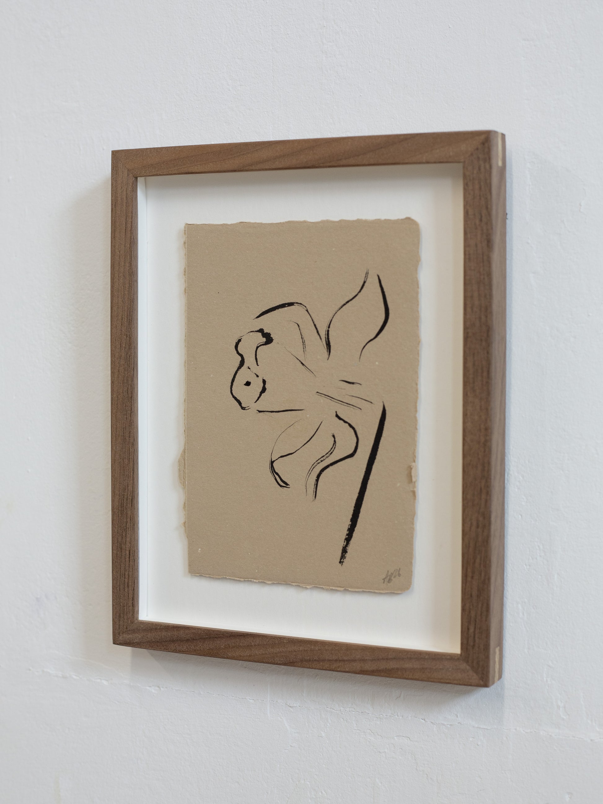Framed artwork of a black line drawing on beige paper against a white wall