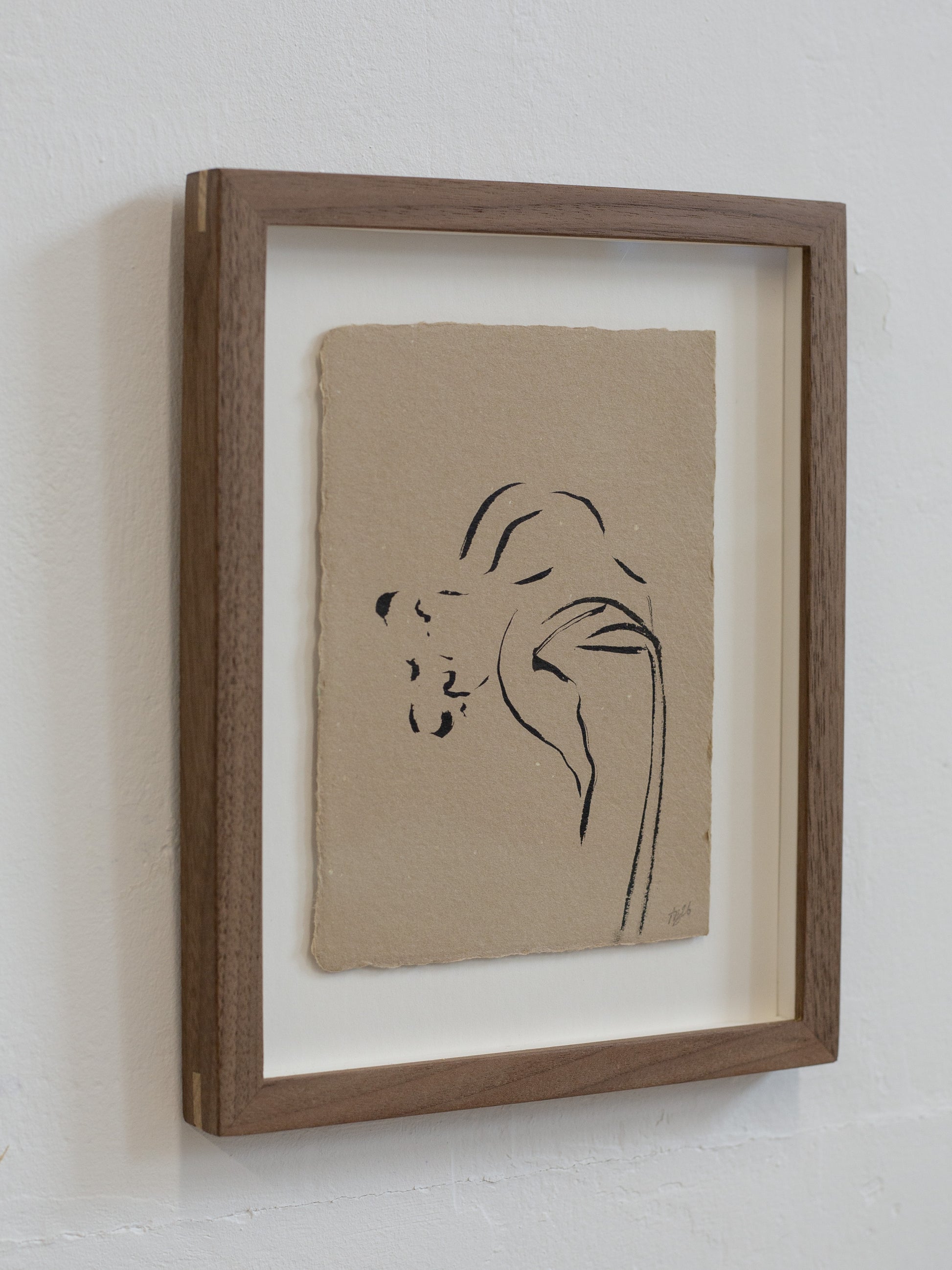 Framed artwork with a minimalist line drawing on beige paper against a white wall.