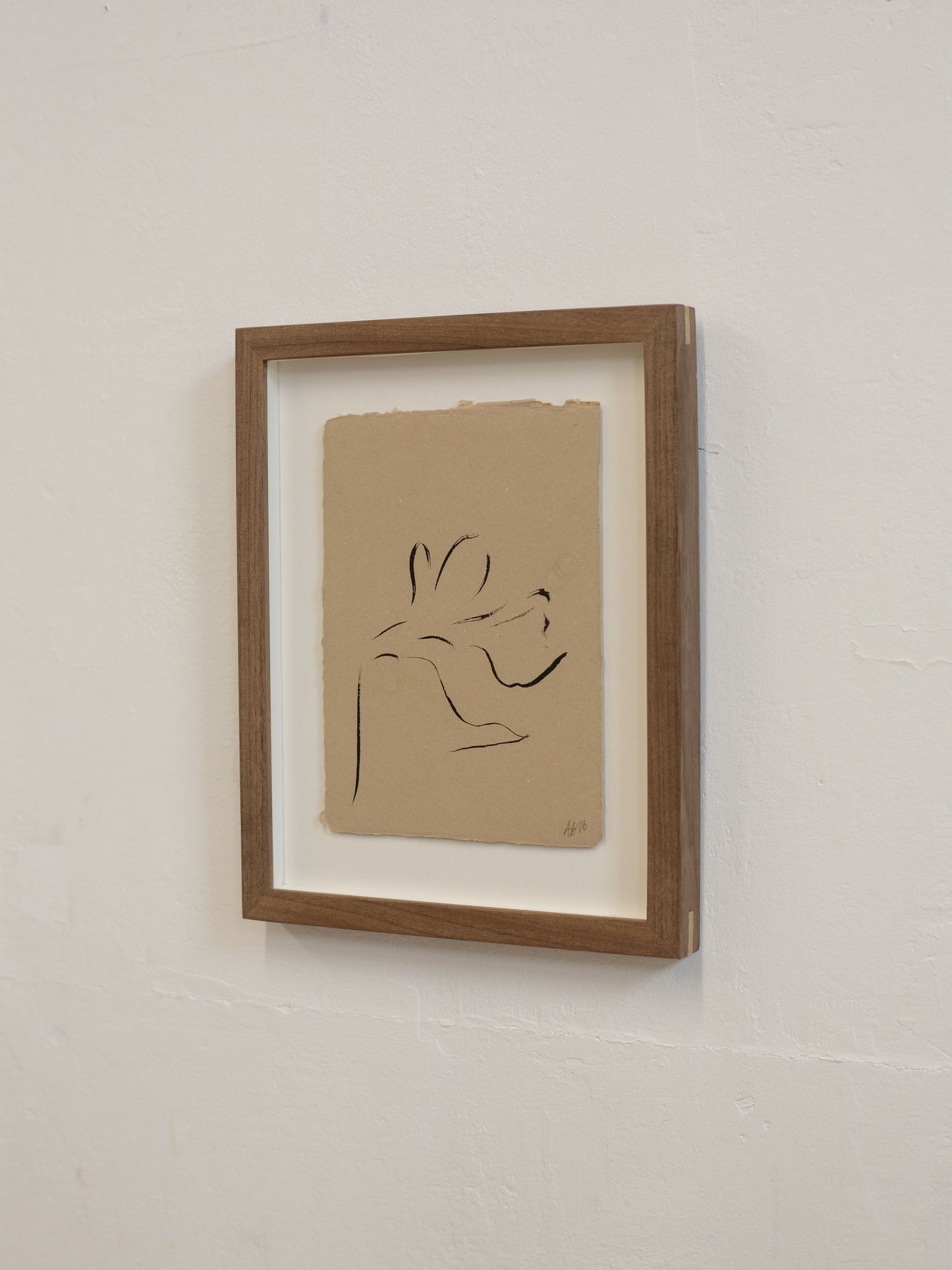 Framed minimalist line drawing on beige paper against a white wall
