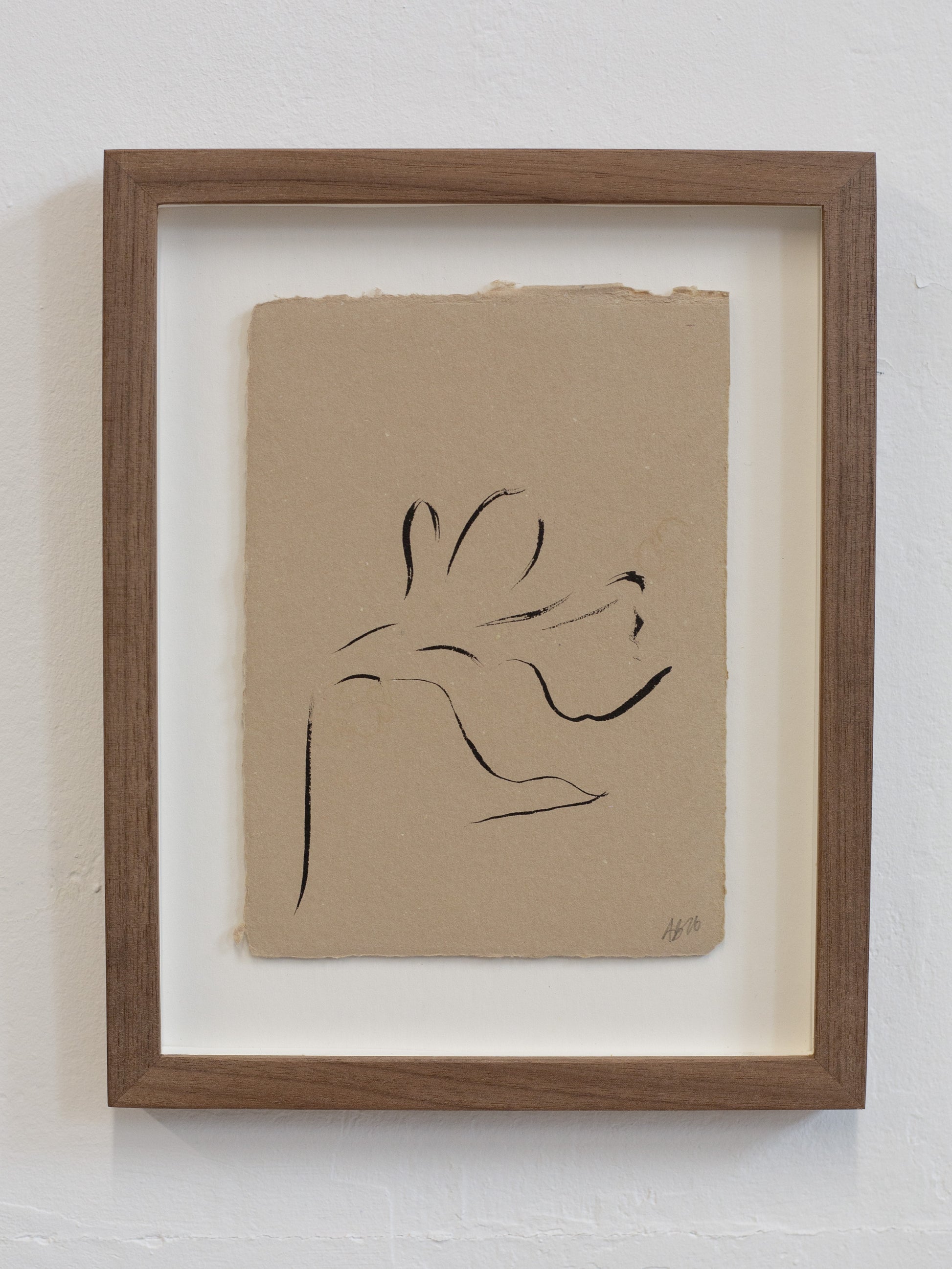 Framed artwork of a black line drawing on beige paper against a white wall.