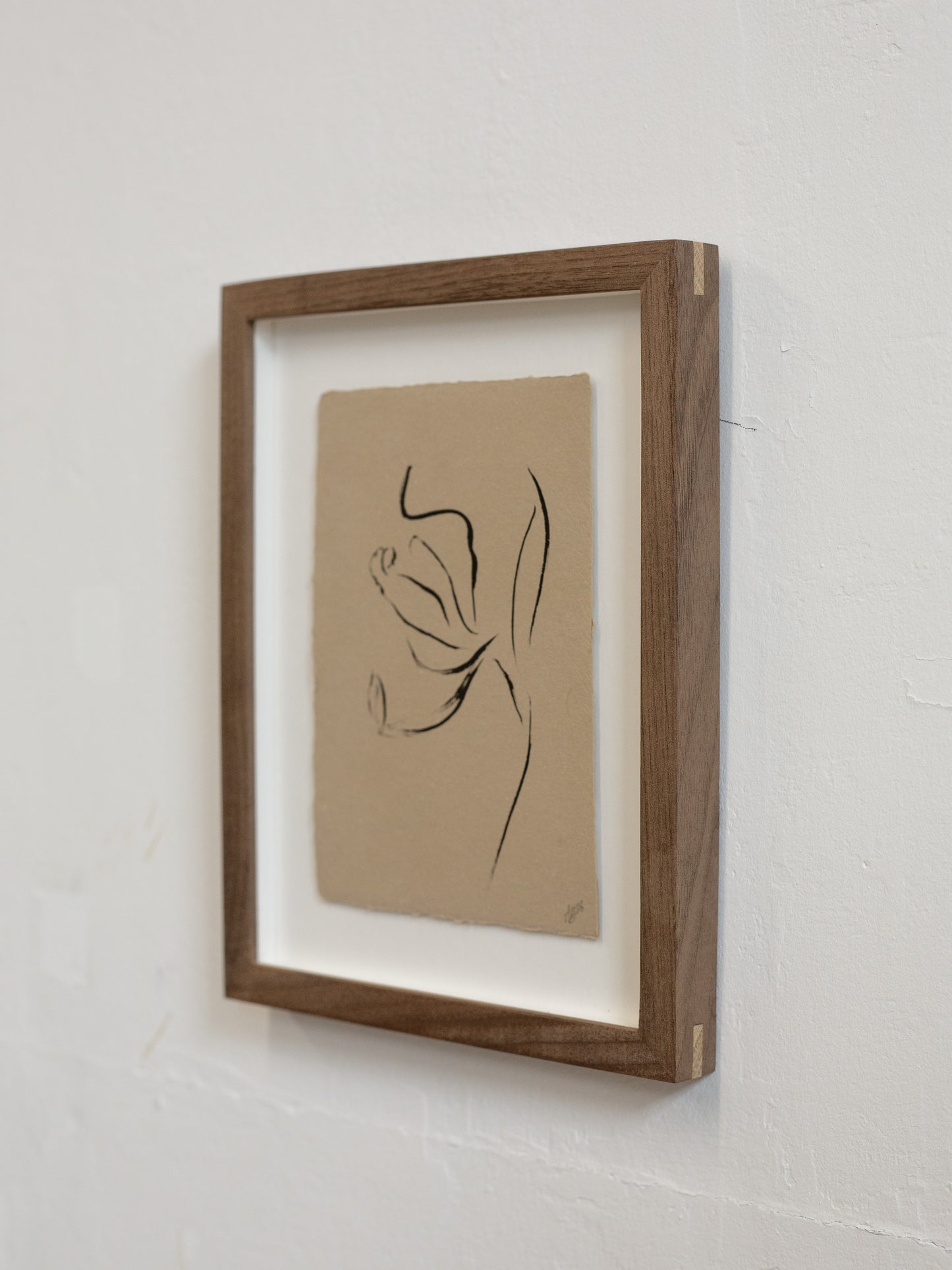 Framed minimalist line art of a flower on a beige background, mounted on a white wall.