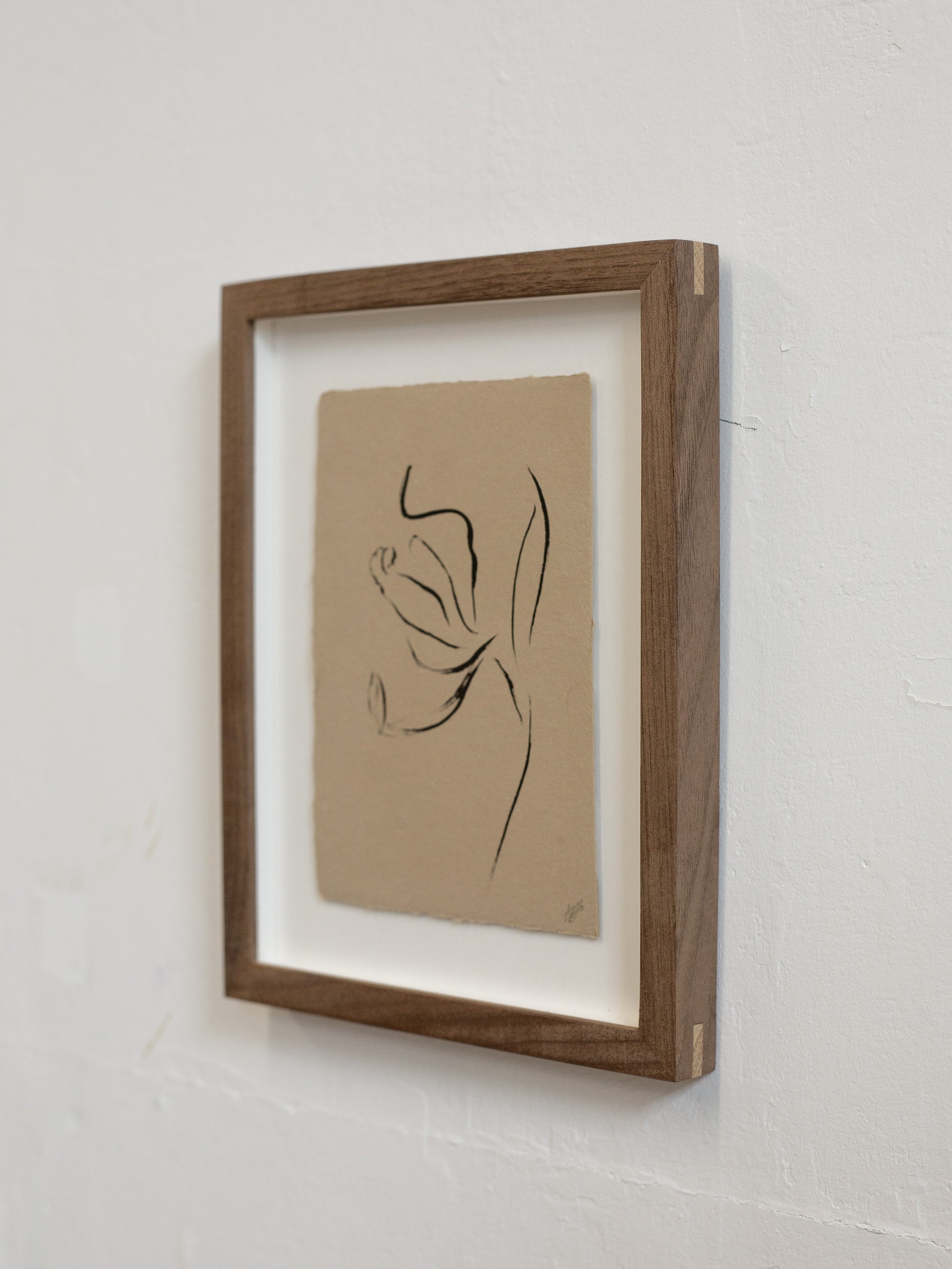 Framed minimalist line art of a flower on a beige background, mounted on a white wall.
