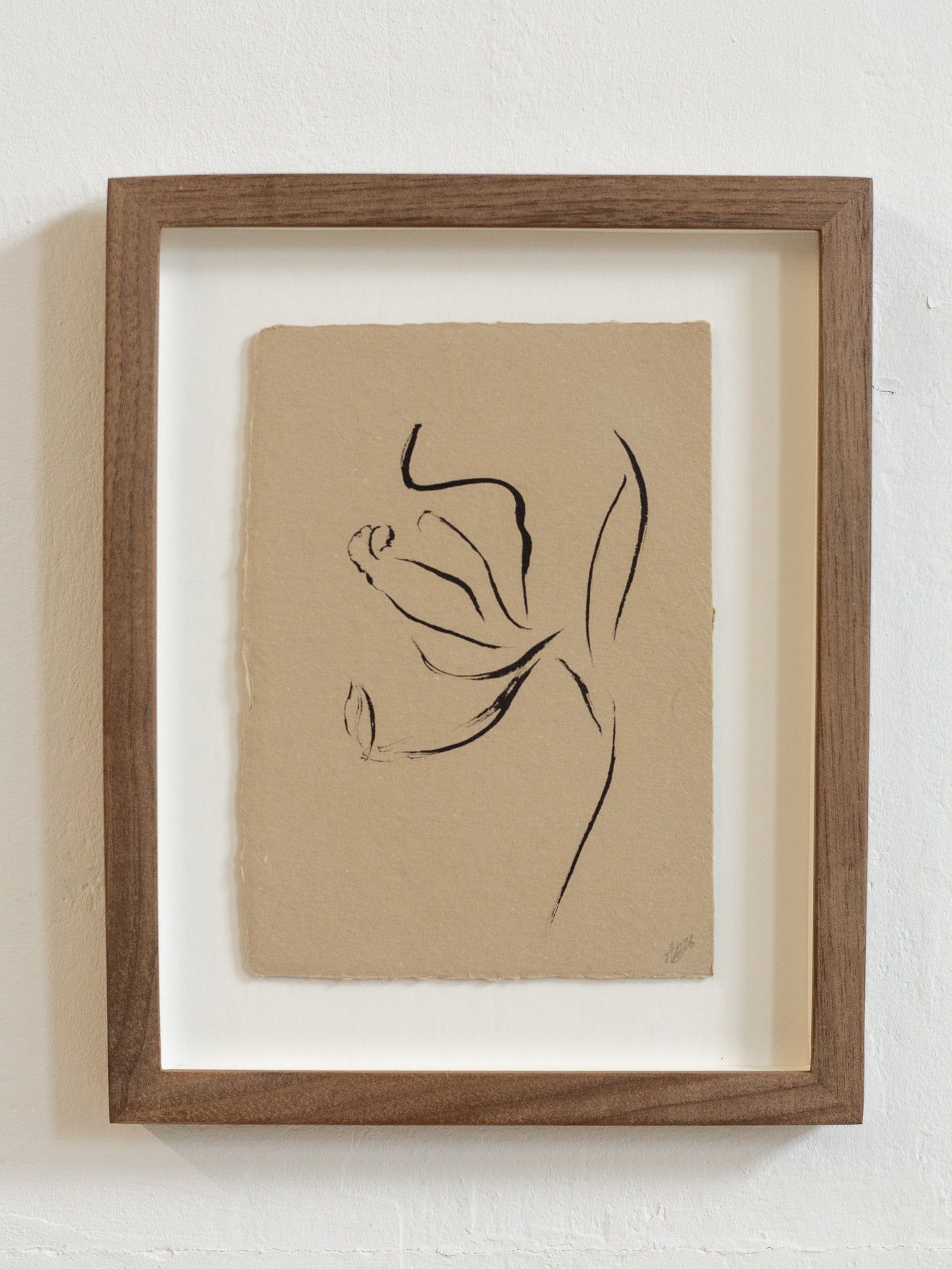 Framed floral abstract black line drawing on beige paper against a white wall