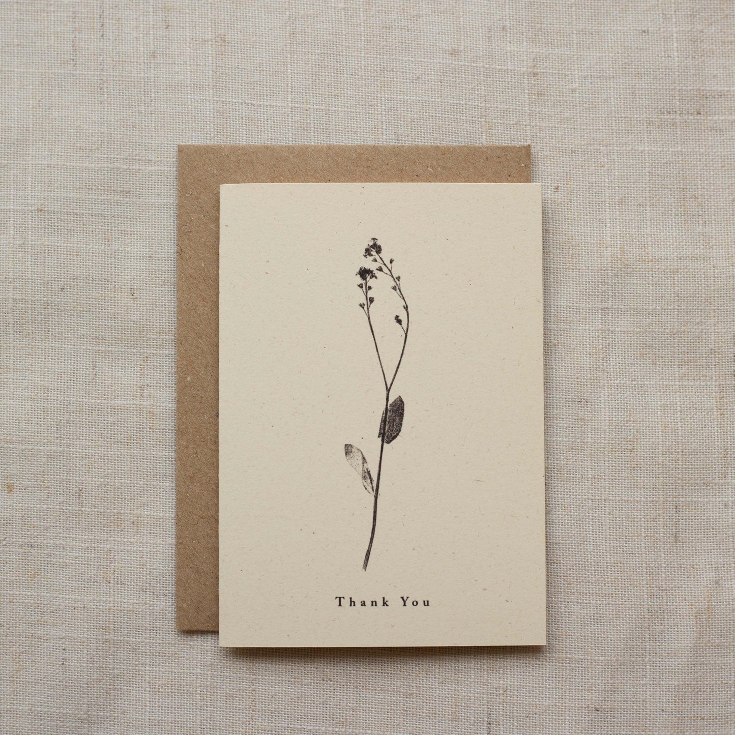 Beige greeting card with plant illustration and 'Thank You' text, placed on a textured beige surface.