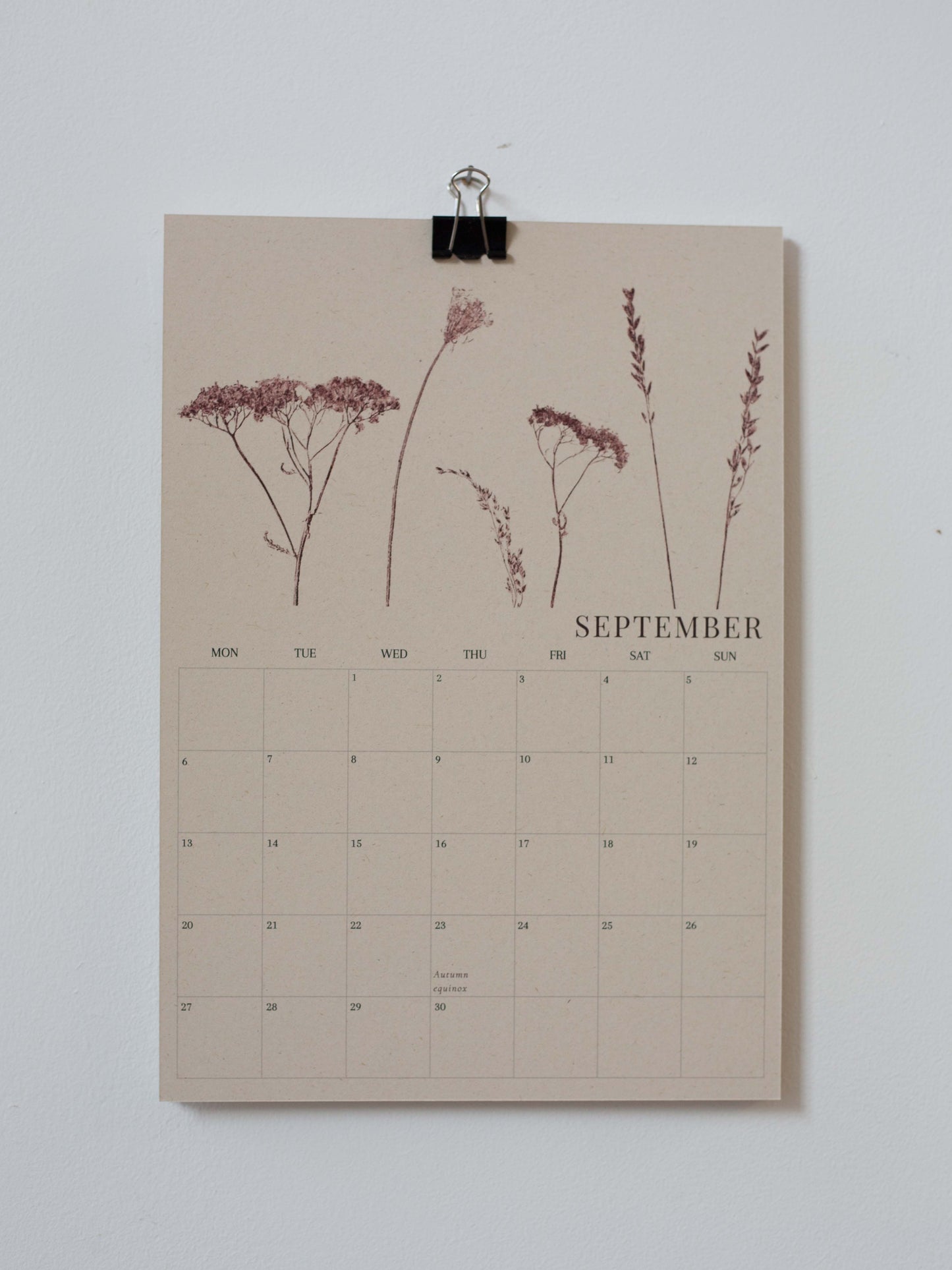 A September wall calendar page with botanical illustrations of wildflowers at the top, clipped to a white wall with a black binder clip.