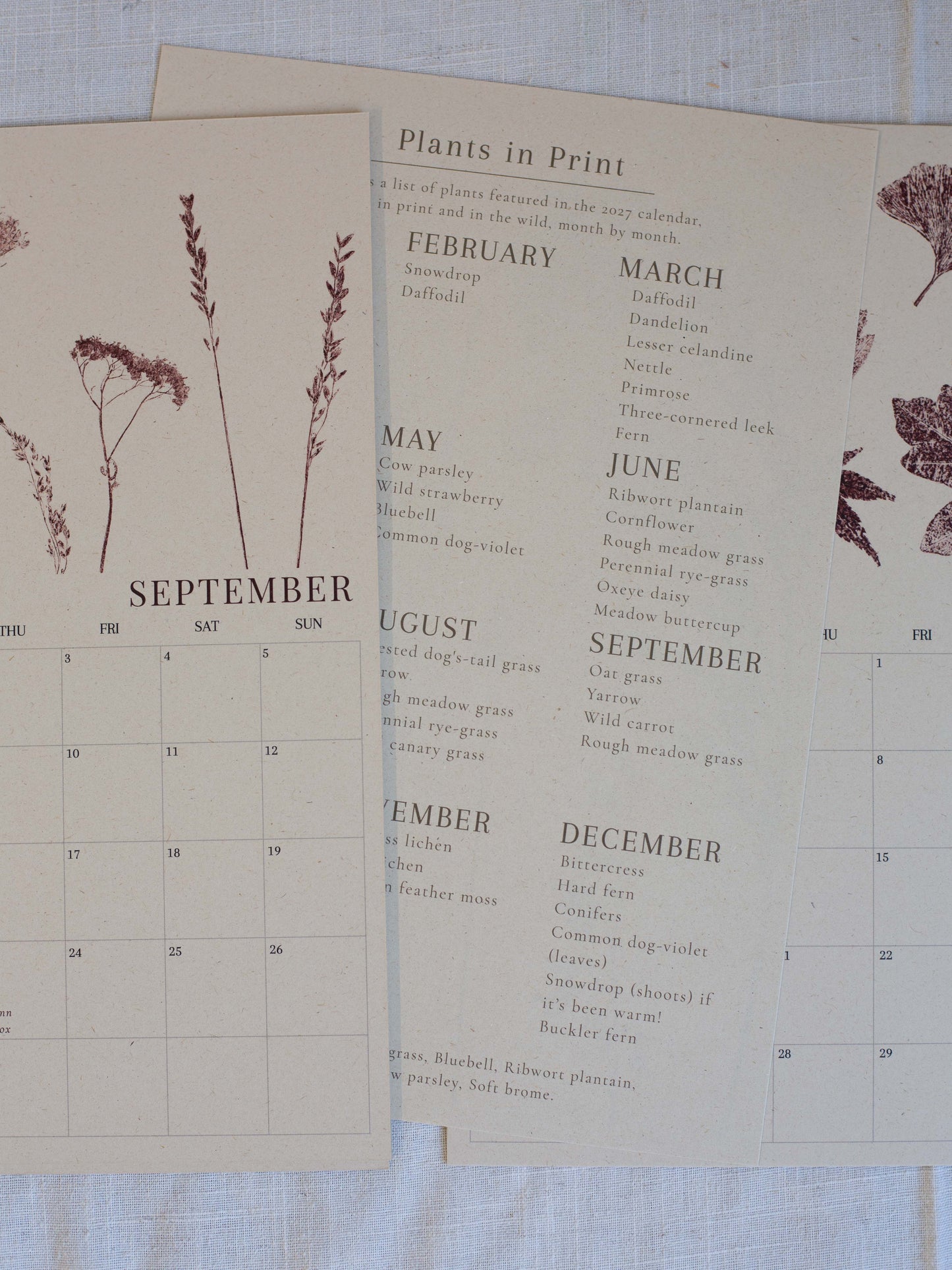 A vintage-style botanical calendar page laid on a light fabric surface, showing months from September to December with printed plant illustrations and a list titled "Plants in Print.".