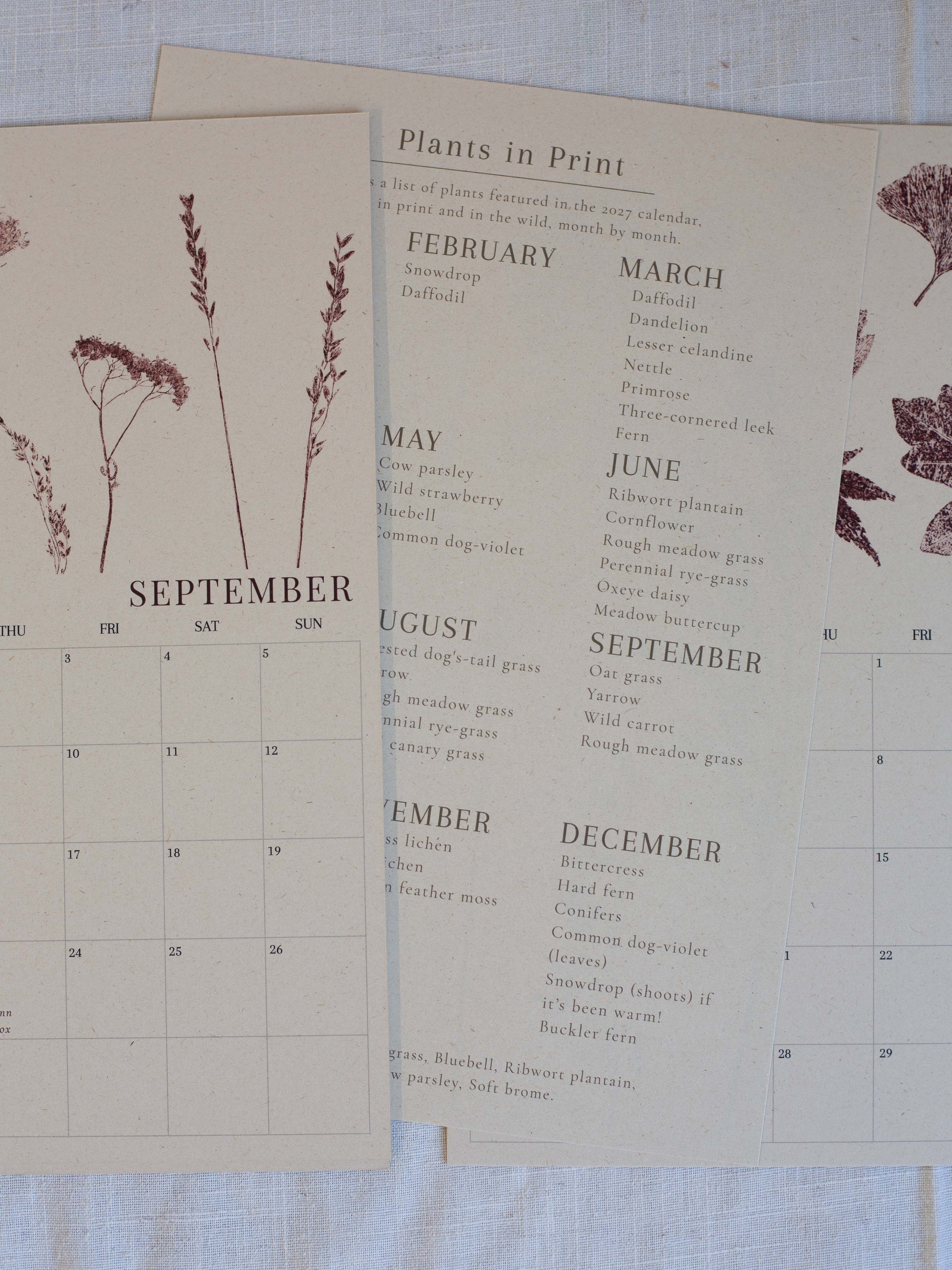 A vintage-style botanical calendar page laid on a light fabric surface, showing months from September to December with printed plant illustrations and a list titled "Plants in Print.".