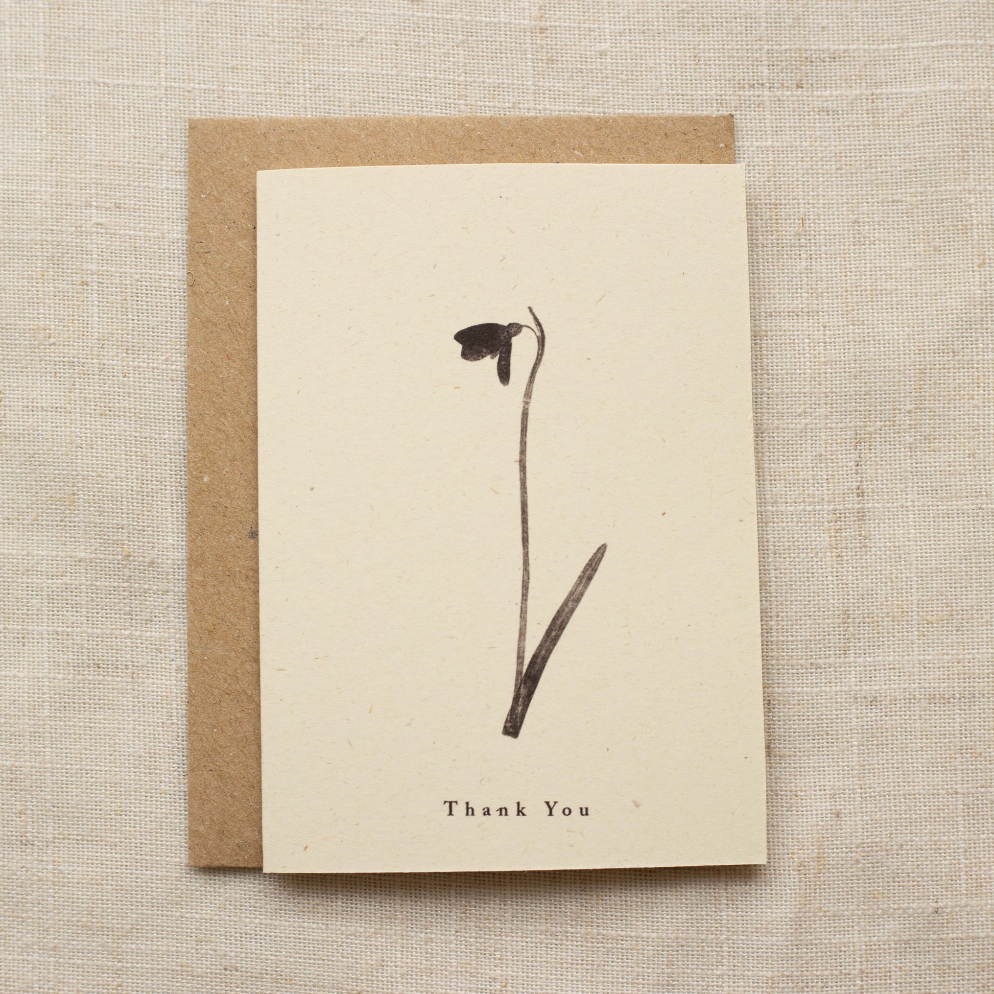 Greeting card with a pressed flower and 'Thank You' text on a beige background
