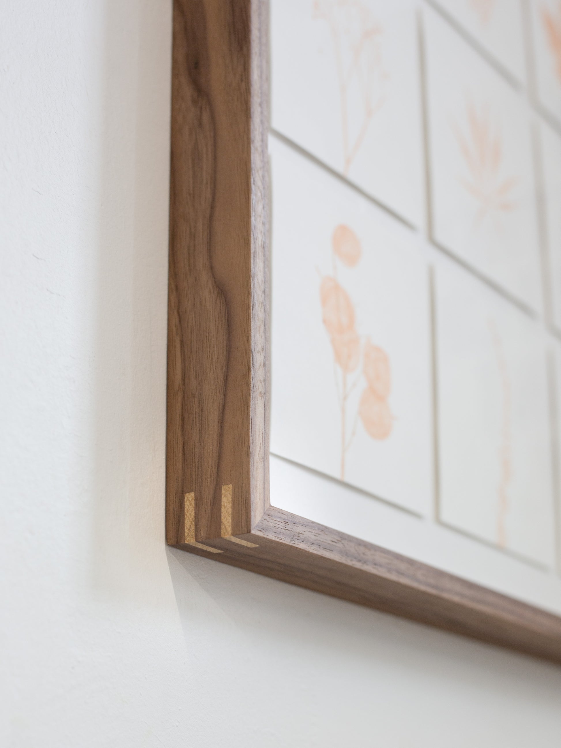 Wooden picture frame on a white wall with floral art in the background
